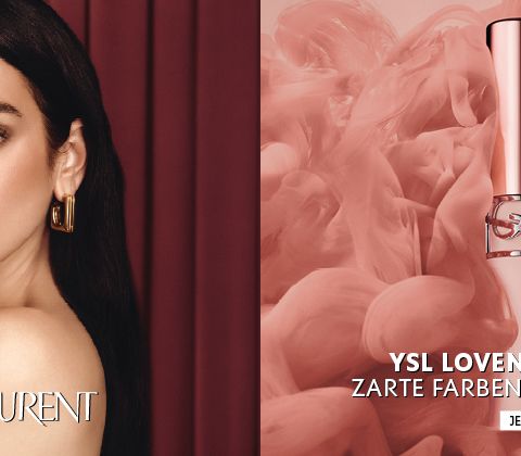 Frau, die einen YSL-Lip-Blusher an die Lippen hält, neben rosa YSL-Lip-Blusher-Flakons vor einem rauchrosa Hintergrund. Text auf Deutsch. YSL-Logo sichtbar.