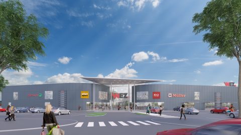 Ein modernes Einkaufszentrum mit mehreren Markenlogos über den Ladenfronten, darunter Spar, Giga Sport und Müller. Der Eingang verfügt über ein großes Vordach und in den umliegenden Straßen parken Autos und Fußgänger. Strahlend blauer Himmel mit einigen Wolken.