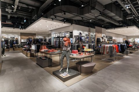 Ein modernes Interieur eines Bekleidungsgeschäfts mit gut organisierten Kleiderauslagen. Schaufensterpuppen im Vordergrund präsentieren lässige Outfits. Helle Beleuchtung und eine neutrale Farbpalette schaffen eine einladende Einkaufsatmosphäre.