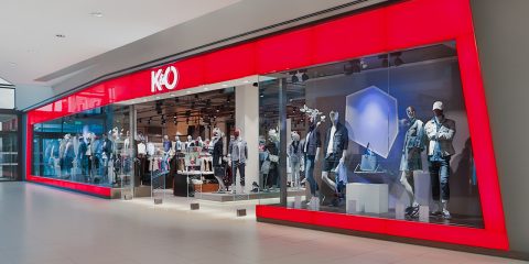 Schaufenster von K&O mit einem rot-weißen Schild und Schaufensterpuppen, die Kleidung im Fenster präsentieren. Der Innenraum ist durch das Glas sichtbar und präsentiert verschiedene Kleidungsstücke und Accessoires. Das Geschäft befindet sich in einem Einkaufszentrum.