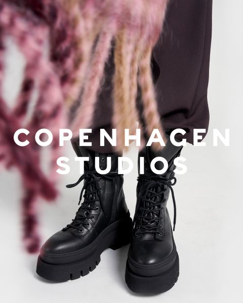 Eine Person in klobigen schwarzen Schnürstiefeln und dunklen Hosen steht auf einer weißen Fläche. Ein Teil des Bildes wird durch rosa und beigefarbenes, unscharfes Garn verdeckt. Der Text "Copenhagen Studios" erscheint über dem Foto.