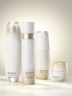 Vier elegante, weiße Sensai Absolute Silk Hautpflegeprodukte, darunter Flaschen und ein Tiegel, sind in einem sanften, leuchtenden Licht angeordnet.