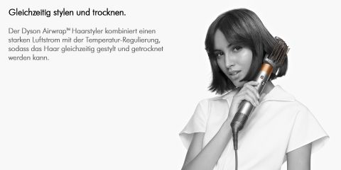 Eine Frau mit schulterlangem Haar benutzt einen Dyson Airwrap™ Styler für ihr Haar. Der Text auf Deutsch hebt die Fähigkeit des Stylers hervor, Haare mit starkem Luftstrom und Temperaturkontrolle gleichzeitig zu stylen und zu trocknen. Der Hintergrund ist hellgrau.