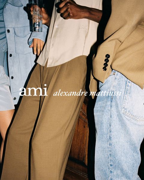Drei eng beieinander stehende Personen in stilvollen Outfits, eine hält ein Getränk in der Hand. Der Text "ami alexandre mattiussi" ist in weißen Buchstaben über das Bild gelegt. Ihre Gesichter sind nicht zu sehen.