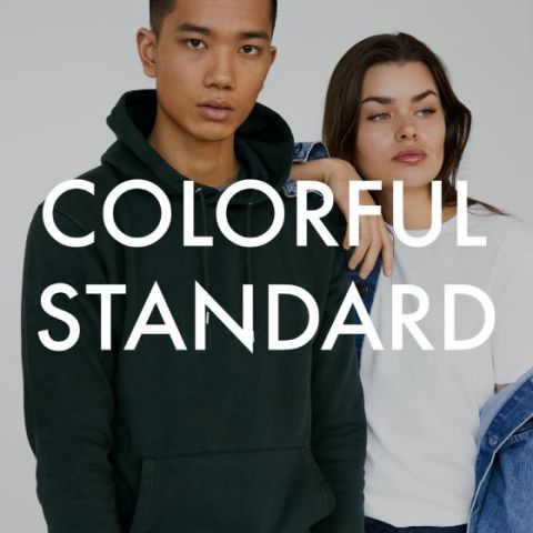Ein Mann und eine Frau posieren zusammen. Der Mann trägt einen dunkelgrünen Kapuzenpullover und die Frau ein weißes T-Shirt mit einer Jeansjacke über den Schultern. Der Text „COLORFUL STANDARD“ ist über das Bild gelegt.