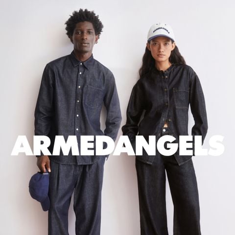Zwei Models in dunklen Jeanshemden und -hosen stehen vor einem weißen Hintergrund mit der Aufschrift "ARMEDANGELS". Ein Modell hält eine blaue Kappe.
