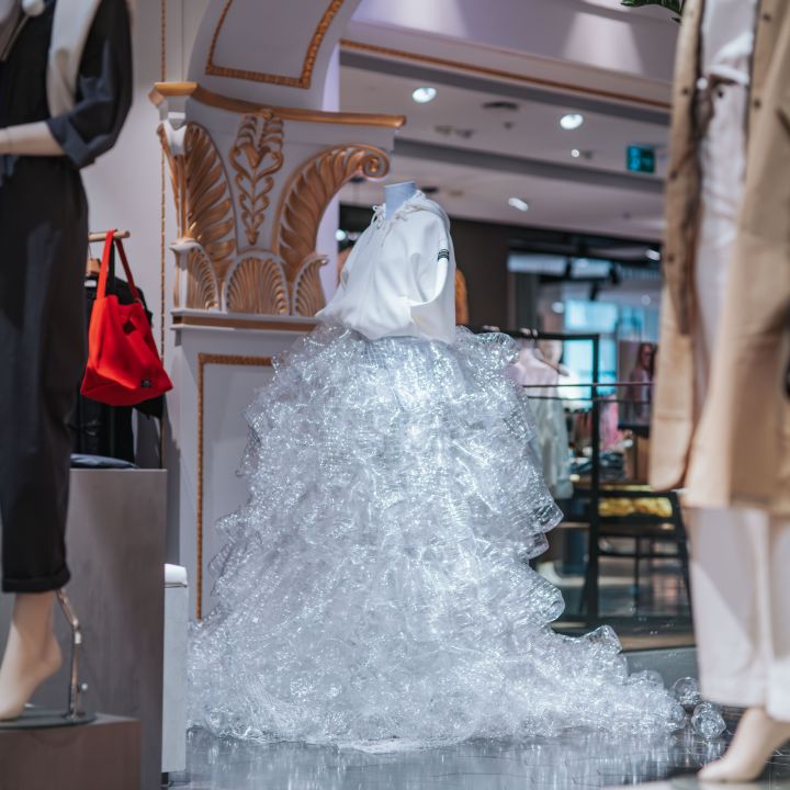 Eine Schaufensterpuppe in einem weißen Oberteil und einem dramatischen Rock aus durchsichtigem Plastik wird in einem stilvollen, verzierten Ladeninneren ausgestellt.