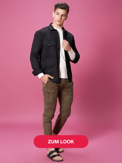 Eine Person posiert vor einem rosa Hintergrund und trägt eine schwarze Jacke, ein weißes Hemd, braune Cargohosen und schwarze Sandalen. Auf einem roten Button an der Unterseite steht „ZUM LOOK“.