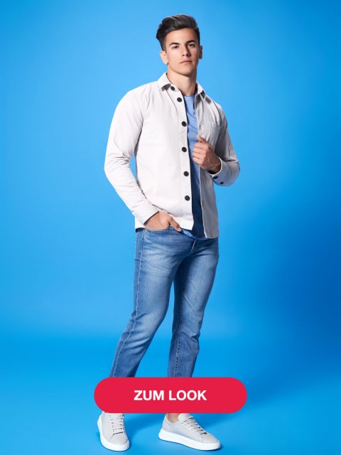 Ein junger Mann steht selbstbewusst vor einem blauen Hintergrund. Er trägt ein weißes Hemd mit Knopfleiste über einem blauen T-Shirt, dazu blaue Jeans und weiße Turnschuhe. Unten ist ein roter „Zum Look“-Button zu sehen.