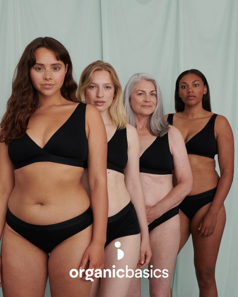 Vier Frauen unterschiedlichen Alters und unterschiedlicher Figur stehen selbstbewusst vor einem hellgrünen Hintergrund, in passender schwarzer Unterwäsche. Am unteren Bildrand steht der Text „organicbasics“.