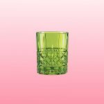 In der Mitte befindet sich ein grüner Glasbecher mit aufwendigem Muster vor einem Hintergrund mit Farbverlauf in zartem Rosa.