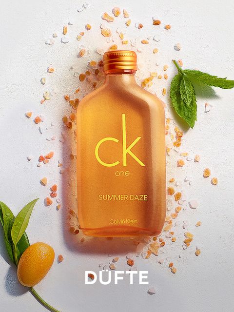 Eine orangefarbene Flasche des Duftes CK One Summer Daze von Calvin Klein liegt auf einer weißen Fläche, umgeben von verstreuten orangefarbenen Kristallen, frischen Minzblättern und einer kleinen Zitrusfrucht. Am unteren Rand ist das Wort „DUFTE“ zu sehen.