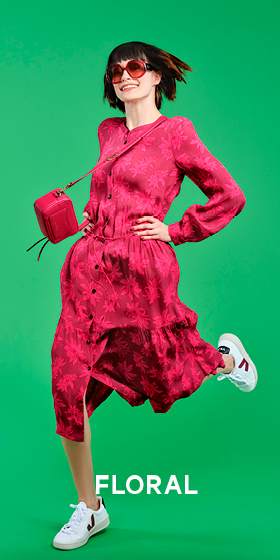 Eine Person in einem roten Blumenkleid und weißen Turnschuhen springt vor einem grünen Hintergrund. Sie hat kurze Haare und trägt eine Sonnenbrille. An ihrer Schulter hängt eine kleine, rote Umhängetasche. Unten steht das Wort „FLORAL“.