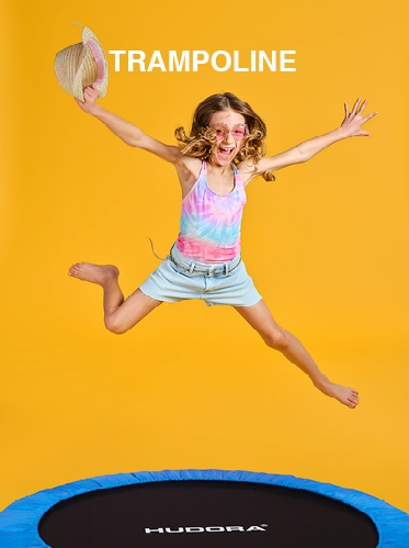 Ein junges Mädchen in Batik-Shirt und Jeansshorts springt fröhlich auf einem Trampolin. Sie trägt eine Sonnenbrille und hält einen Strohhut. Der Hintergrund ist leuchtend gelb und über ihr steht das Wort „TRAMPOLIN“.