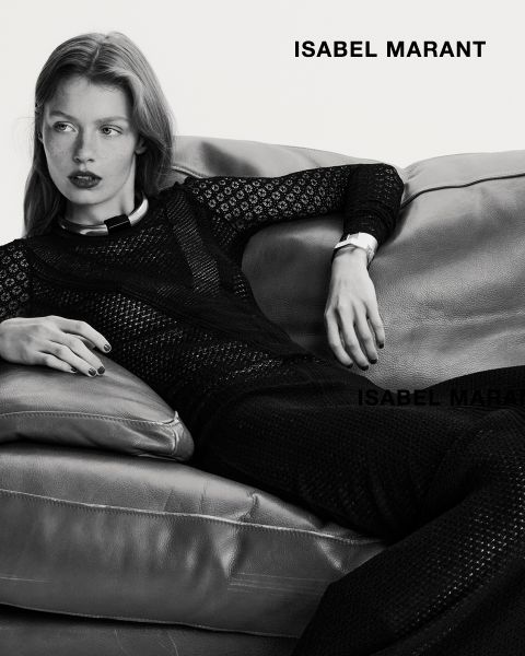 Eine Frau liegt auf einem Ledersofa und trägt ein langärmeliges, strukturiertes schwarzes Outfit. Das Bild ist in Schwarz-Weiß gehalten, mit dem Schriftzug "ISABEL MARANT" in fetten Buchstaben in der rechten oberen und unteren Ecke.