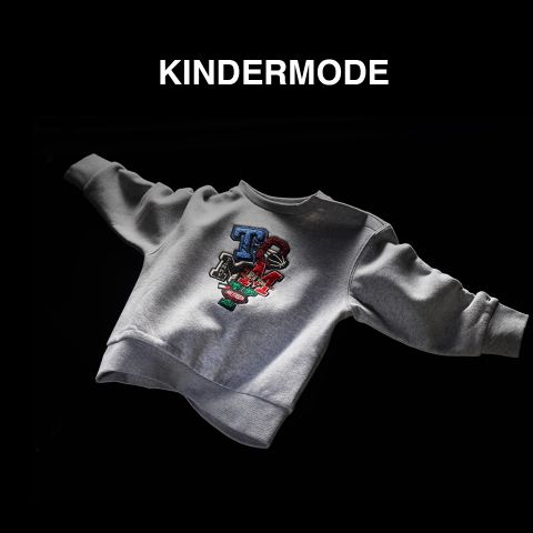 Auf schwarzem Hintergrund ist ein graues Kindersweatshirt mit einem bunten, cartoonhaften Text auf der Vorderseite zu sehen. Über dem Sweatshirt steht der Schriftzug „KINDERMODE“.