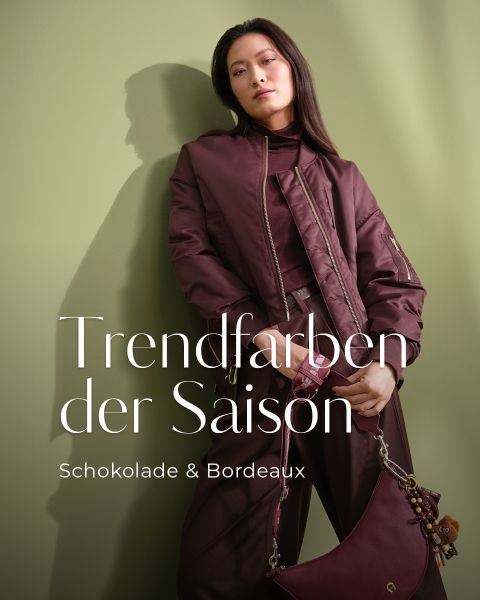 Eine Frau posiert vor einem blassgrünen Hintergrund und trägt mehrschichtige Kleidung und Accessoires in tiefen Schokoladen- und Bordeaux-Tönen. Der weiße Text lautet: "Trendfarben der Saison. Schokolade & Bordeaux.