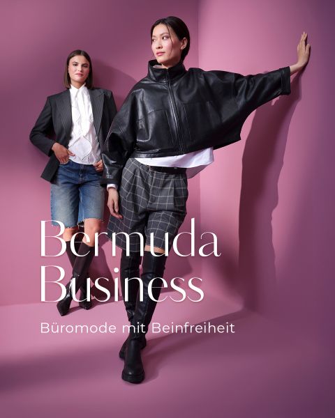 Zwei Frauen posieren vor einem rosafarbenen Hintergrund und tragen moderne Business-Outfits mit Bermudashorts; eine trägt einen schwarzen Blazer und Jeans-Shorts, die andere eine schwarze Lederjacke mit karierten Bermudashorts. Der weiße Text lautet "Bermuda Business".