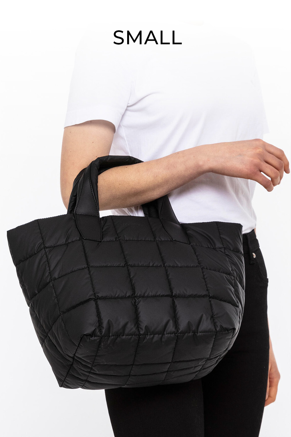 Person hält eine kleine, schwarze, gesteppte Handtasche. Sie trägt ein weißes Hemd und eine schwarze Hose. Über der Tasche steht das Wort „SMALL“.