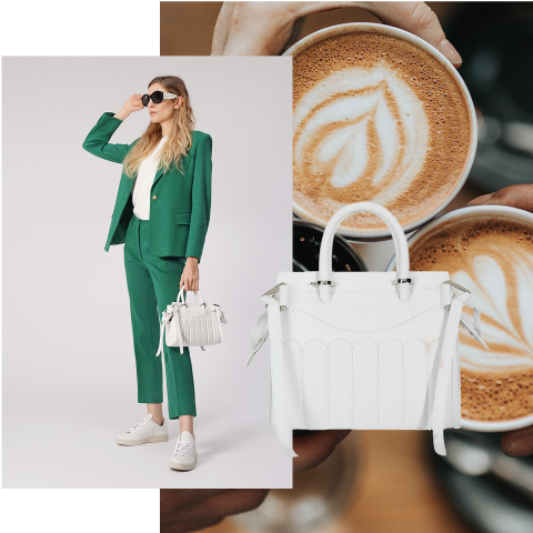 Eine Frau im grünen Anzug posiert mit einer weißen Handtasche, trägt Sonnenbrille und Turnschuhe. Neben der Handtasche stehen zwei Tassen Kaffee mit Latte Art.