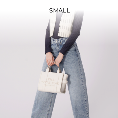 Person hält eine weiße Einkaufstasche mit dem Aufdruck „THE TOTE BAG“. Sie trägt ein marineblaues Langarmhemd, eine weiße Nadelstreifenweste und hellblaue Jeans mit weitem Bein. Darüber steht das Wort „SMALL“.