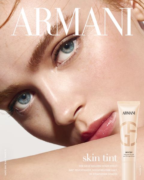 Nahaufnahme eines Modells mit heller Haut und blauen Augen, das eine taufrische, strahlende Haut zeigt. In der unteren rechten Ecke ist eine Tube Armani-Hautfarbe abgebildet, deren Text für 24-Stunden-Hydratation und 20 strahlende Farbtöne wirbt.