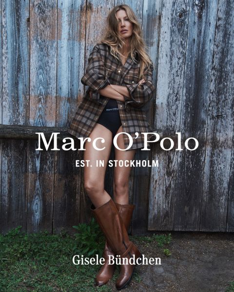 Eine Frau in einem karierten Hemd, schwarzen Shorts und braunen Stiefeln steht vor einer verwitterten Holzwand. Der Text lautet: "Marc O'Polo EST. IN STOCKHOLM Gisele Bündchen.