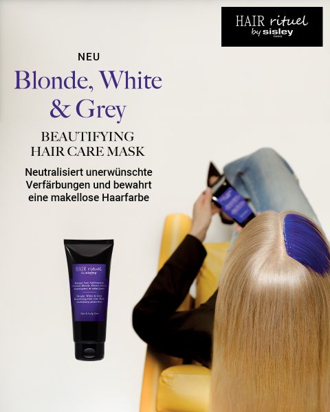 Eine Frau mit langen blonden Haaren, blauen Strähnchen und einem gelben Stuhl liest, während sie eine Tube Sisley-Haarmaske in der Hand hält; Produktdetails werden angezeigt.