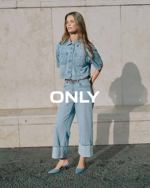 Eine junge Frau in einem schwarzen Mantel, einem blau gestreiften Hemd und einem kastanienbraunen Rock geht auf einer Straße in der Stadt mit historischen Gebäuden im Hintergrund. Das Wort "ONLY" wird quer über das Bild angezeigt.