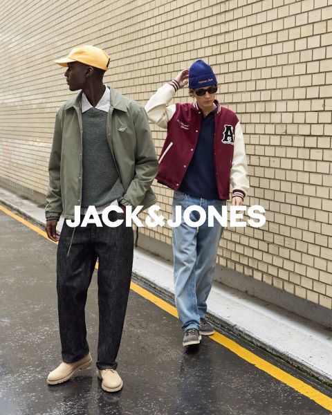 Zwei Männer in Jeans-Outfits sitzen vor einem schlichten Hintergrund. Der vordere Mann hält sich die Hand auf den Mund, während der andere hinter ihm sitzt. In der Mitte steht der Text "JACK & JONES".