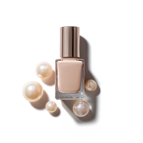 Ein nudefarbenes Nagellackfläschchen mit einer Metallkappe steht neben mehreren glänzenden, cremefarbenen Perlen auf weißem Hintergrund.