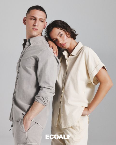 Eine Person, die einen schwarzen, gesteppten Wintermantel trägt, steht vor einem schlichten, hellen Hintergrund. Das Wort "ECOALF" ist deutlich in der Mitte des Bildes zu lesen.