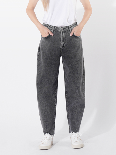 Eine Person, die eine hoch taillierte, locker sitzende, verwaschene schwarze Jeans mit den Händen in den Taschen trägt, gepaart mit einem weißen T-Shirt und weißen Turnschuhen, steht vor einem schlichten hellen Hintergrund.