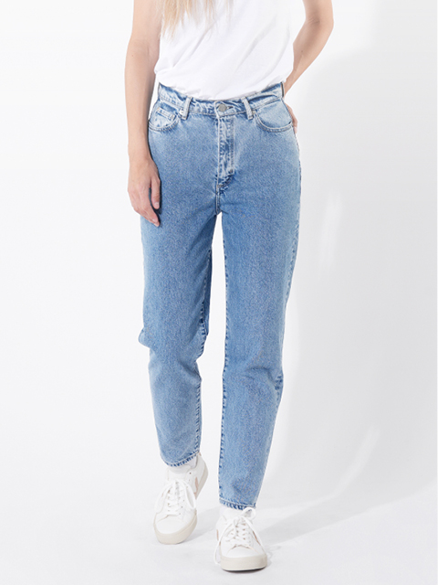 Eine Person, die hellblaue Jeans mit hoher Taille, ein weißes T-Shirt und weiße Turnschuhe trägt, steht vor einem schlichten weißen Hintergrund. Ihre linke Hand ruht auf ihrer Hüfte, während ihr rechter Arm an ihrer Seite herunterhängt.