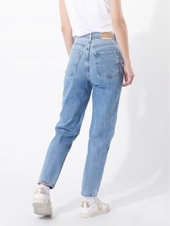 Eine Person, die hellblaue Jeans mit hoher Taille, ein weißes T-Shirt und weiße Turnschuhe trägt, steht vor einem schlichten weißen Hintergrund. Ihre linke Hand ruht auf ihrer Hüfte, während ihr rechter Arm an ihrer Seite herunterhängt.