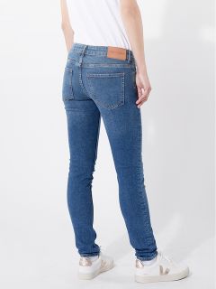 Eine Person, die eine blaue Röhrenjeans, ein weißes T-Shirt und weiße Turnschuhe trägt, steht vor einem schlichten weißen Hintergrund. Das Gesicht der Person ist nicht zu sehen; nur der Körper von den Schultern abwärts ist abgebildet.