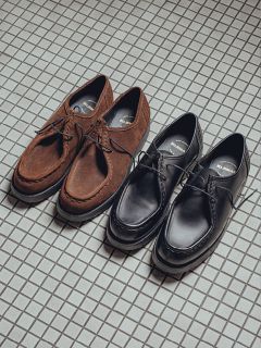 Zwei Paar Schnürschuhe stehen nebeneinander auf einem gefliesten Boden: ein Paar aus braunem Wildleder und das andere aus schwarzem Leder. Beide Schuhe haben ein ähnliches Design im Mokassin-Stil.