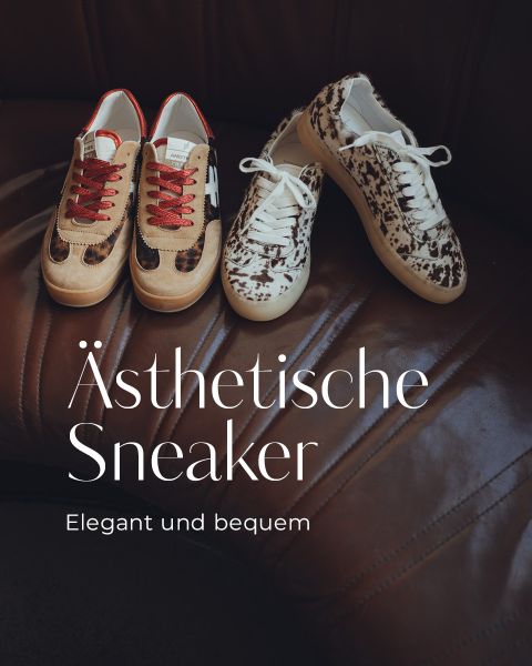 Zwei Paar modische Turnschuhe mit Rindsledermuster, eines mit roten und eines mit weißen Schnürsenkeln, stehen auf einem braunen Ledersofa. Der deutsche Text lautet: "Ästhetische Sneaker. Elegant und bequem.