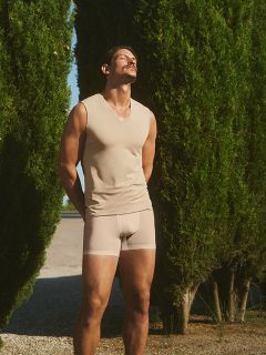 Eine Frau in einem roten Kleid und einer herzförmigen Sonnenbrille sitzt auf einem weißen Stuhl, umgeben von bunten Blumen, darunter Rosen, Gänseblümchen und Lilien. Die Umgebung scheint ein nächtlicher Außenbereich zu sein.