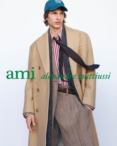 Drei eng beieinander stehende Personen in stilvollen Outfits, eine hält ein Getränk in der Hand. Der Text "ami alexandre mattiussi" ist in weißen Buchstaben über das Bild gelegt. Ihre Gesichter sind nicht zu sehen.