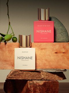 Ein Flakon des Parfums "Hundred Silent Ways" von Nishane mit einer goldenen Kappe, die sich unten spiegelt, und einem verschwommenen roten und schwarzen Hintergrund.