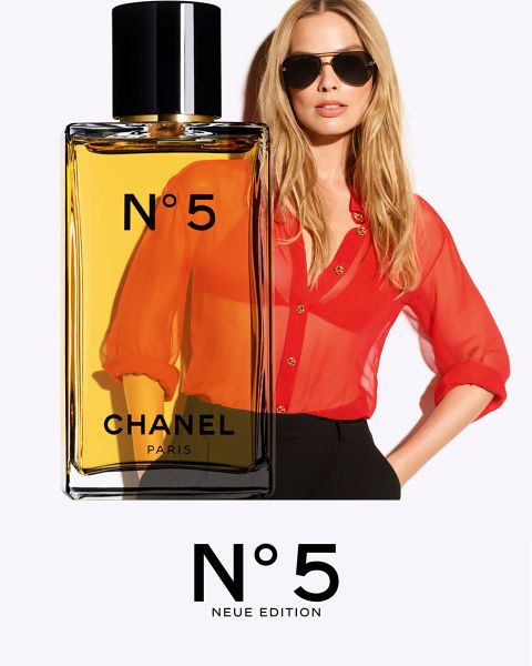 Eine lächelnde Frau in rosafarbener Jacke und schwarzem Rock springt neben einer großen Flasche des Parfums CHANEL Chance Eau Splendide auf weißem Hintergrund.