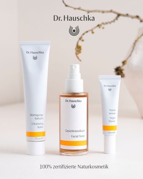 Das Bild zeigt verschiedene Hautpflegeprodukte von Dr. Hauschka, darunter Cremes und Öle, sowie natürliche Elemente wie Blumen und Samen. Der Text lautet: „100 % zertifizierte Naturkosmetik. Natürlich. Anders. Wirksam.“.