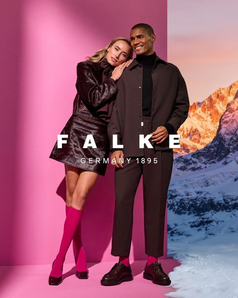 Ein Modell in einem kastanienbraunen Blazer, braunen Handschuhen, einer grünen Strumpfhose, einem grauen Rock mit hohen Schlitzen und braunen Ankle Boots posiert vor einem geometrischen Hintergrund. Der Text lautet "FALKE GERMANY 1895".