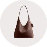 Tote Tasche aus braunem Wildleder mit doppelten Henkeln und einem kleinen metallischen Akzent auf der Vorderseite auf weißem, kreisförmigem Hintergrund.