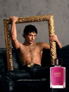 Eine Flasche JOOP! Homme Le Parfum wird vor einem unscharfen Hintergrund mit einer violetten Irisblüte gehalten. Das goldene Logo von „JOOP!“ ist oben deutlich zu erkennen. Das Bild vermittelt Eleganz und Luxus.