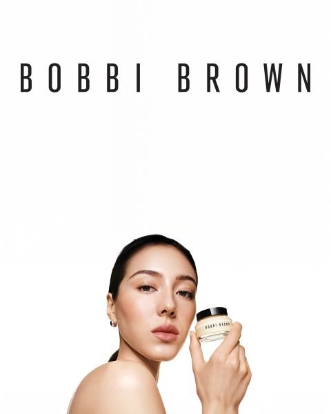 Eine Auswahl langanhaltender Creme-Lidschattenstifte von Bobbi Brown in verschiedenen Farbtönen, horizontal auf einer strukturierten Oberfläche präsentiert. Jeder Stift ist geöffnet und gibt die cremigen Farben frei. Der Markenname ist auf den Kappen sichtbar.