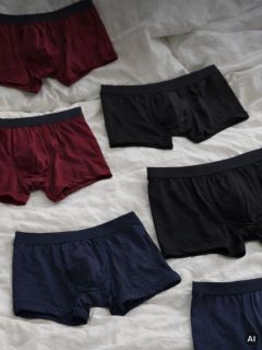 Sechs Paar Boxershorts für Herren in den Farben Schwarz, Burgunderrot und Marineblau liegen auf einer weißen Stoffunterlage ausgebreitet.