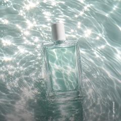 Ein rechteckiger Parfümflakon aus Glas mit weißem Verschluss schwimmt auf glitzerndem, sonnenbeschienenem Wasser.