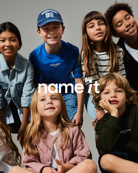 Eine Gruppe von acht verschiedenen Kindern steht vor einem grauen Hintergrund zusammen, alle tragen lässige, aufeinander abgestimmte Outfits in neutralen und Pastellfarben. Der Text "name it" erscheint in der Mitte des Bildes.